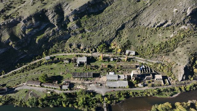 Vista alta casi frontal del conjunto de Vegamediana: cubiertas, muros abiertos, chimeneas, cuatro estructuras circulares junto a la ladera, patios y río en primer plano.