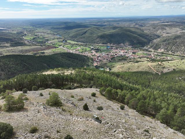 Cistierna y vega al fondo, bosque y claro pedregoso delante; pequeña plataforma con atril del mirador en el borde inferior.